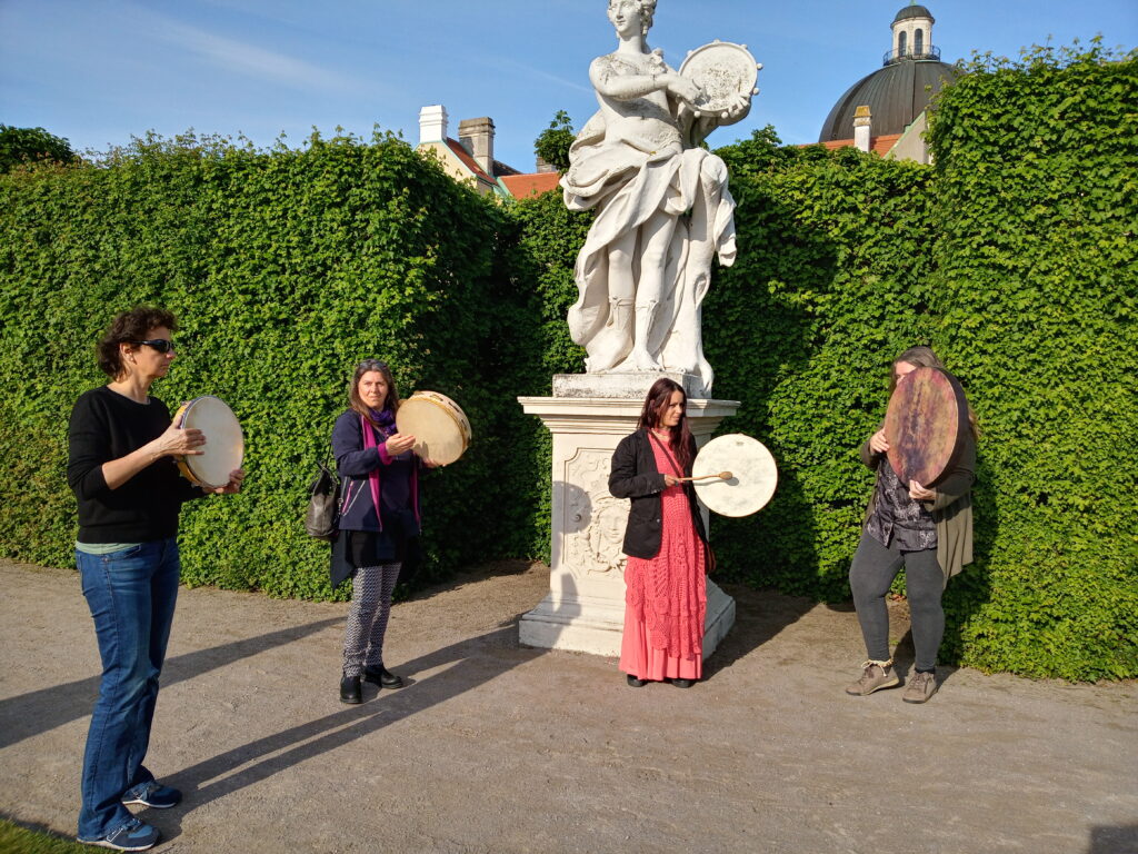 Zwei Frauen spielen Rahmentrommel bei der Statue der Rahmentrommel spielenden Muse Terpsichore im Belevedere Park Wiens.