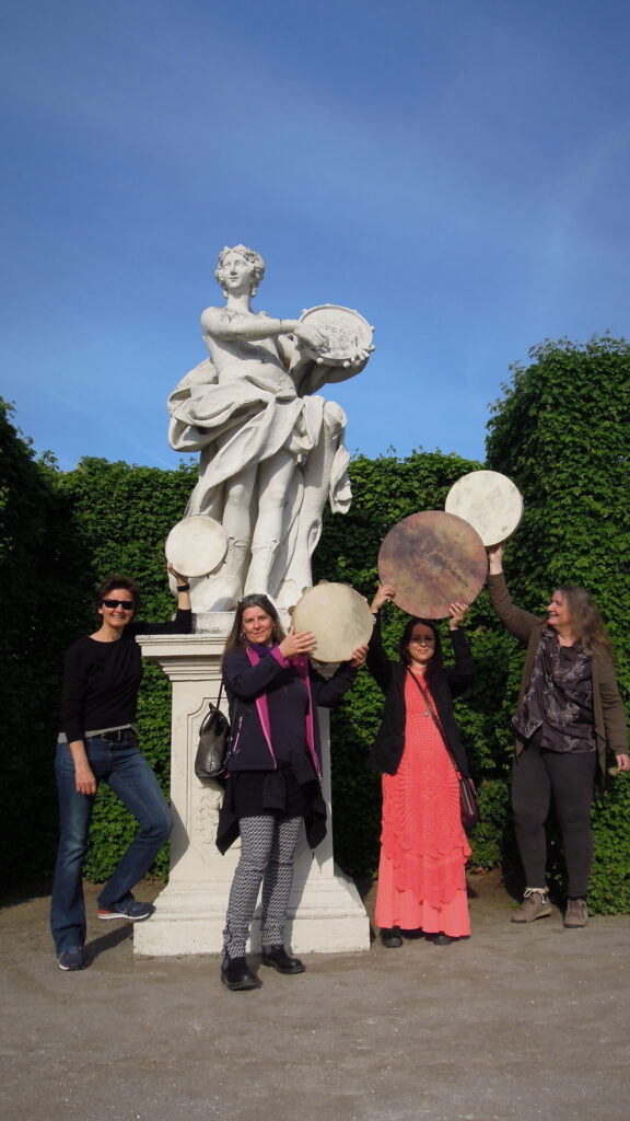 Vier Rhythm Sistas Unlocked mit Karin Bindu posieren mit Rahmentrommel bei der Statue der Rahmentrommel spielenden Muse Terpsichore im Belevedere Park Wiens.