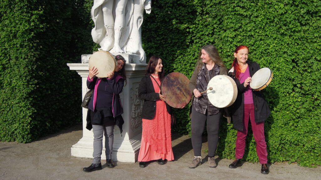 Vier Rhythm Sistas Unlocked mit Karin Bindu posieren mit Rahmentrommel bei der Statue der Rahmentrommel spielenden Muse Terpsichore im Belevedere Park Wiens.